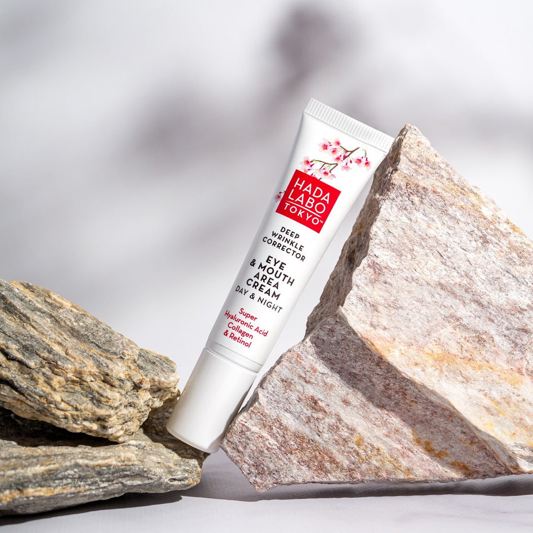 HADA LABO Deep Wrinkle Corrector Eye & Mouth Area Cream 15ml upprätt mellan två strukturerade stenar.