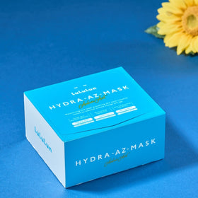 LuLuLun Hydra AZ-Mask Sheet Mask placerad på blått underlag bredvid en gul konstgjord solros.