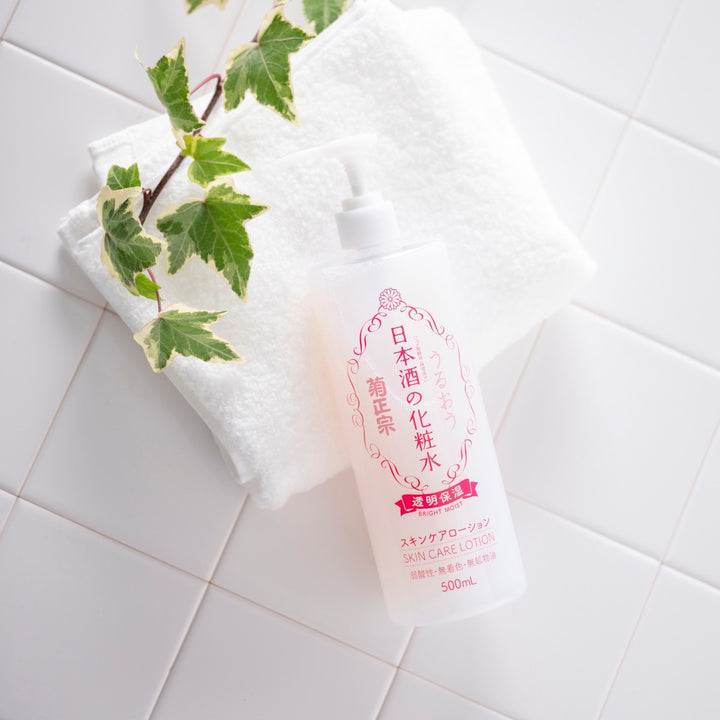KIKU-MASAMUNE Sake Bright Moist Skin Care Lotion 500ml placerad på vit handduk bredvid gröna blad på vita kakelplattor.