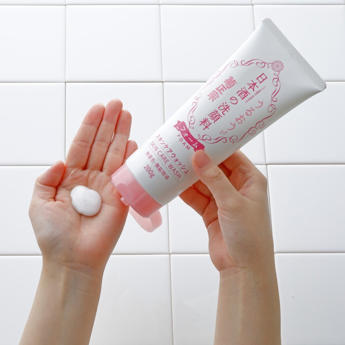 En person trycker ut KIKU-MASAMUNE Sake Skin Care Foaming Face Wash i handen framför vita kakelväggar.
