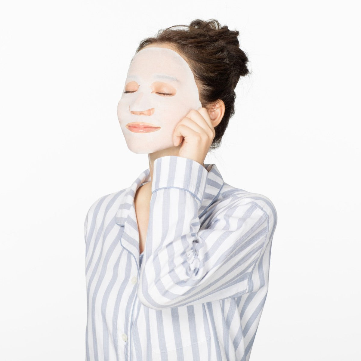 Person i randiga pyjamas applicerar Saborino Morning Facial Sheet Mask Minty Fresh N 32st med slutna ögon.